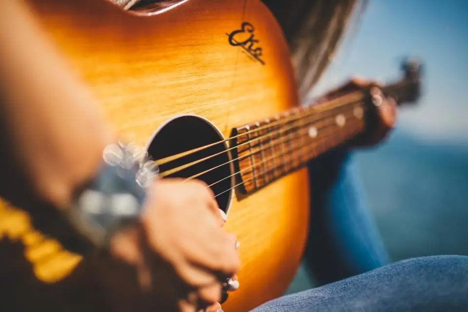 Le mani di un musicista sulle corde di una chitarra acustica, alla luce del giorno