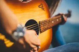 Le mani di un musicista sulle corde di una chitarra acustica, alla luce del giorno
